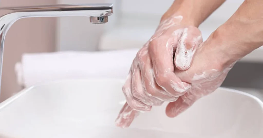 Person washing hands with soap lather under faucet for pink eye prevention, proper handwashing hygiene to prevent conjunctivitis spread.