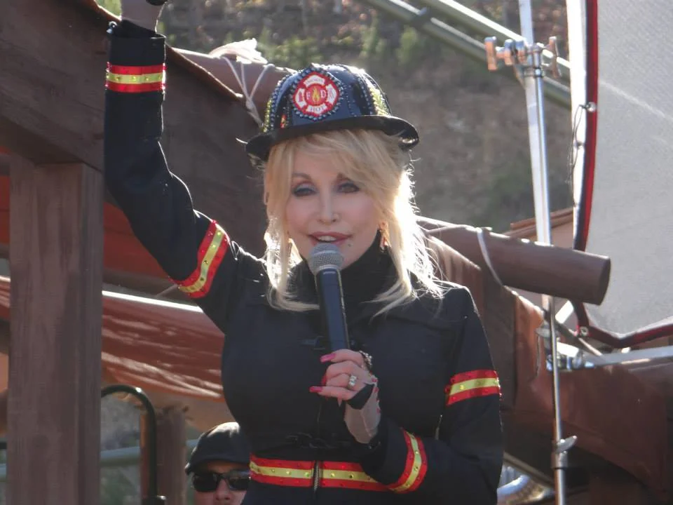 Dolly Parton wearing firefighter helmet speaking at community event