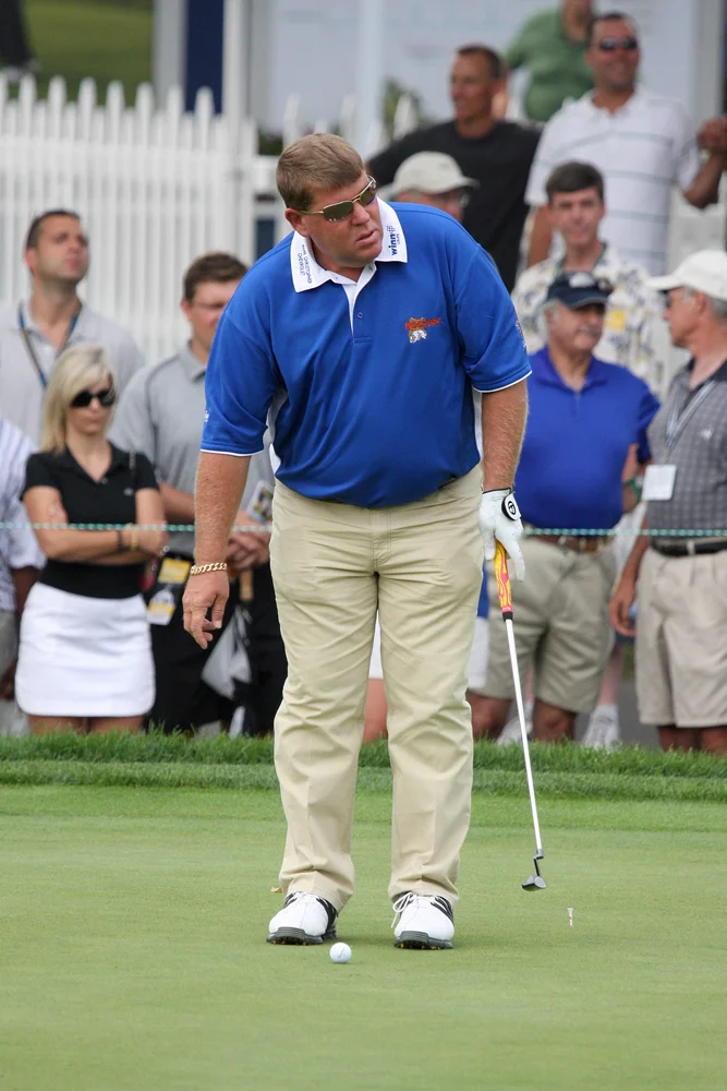 John Daly putting on green at PGA tournament wearing blue shirt