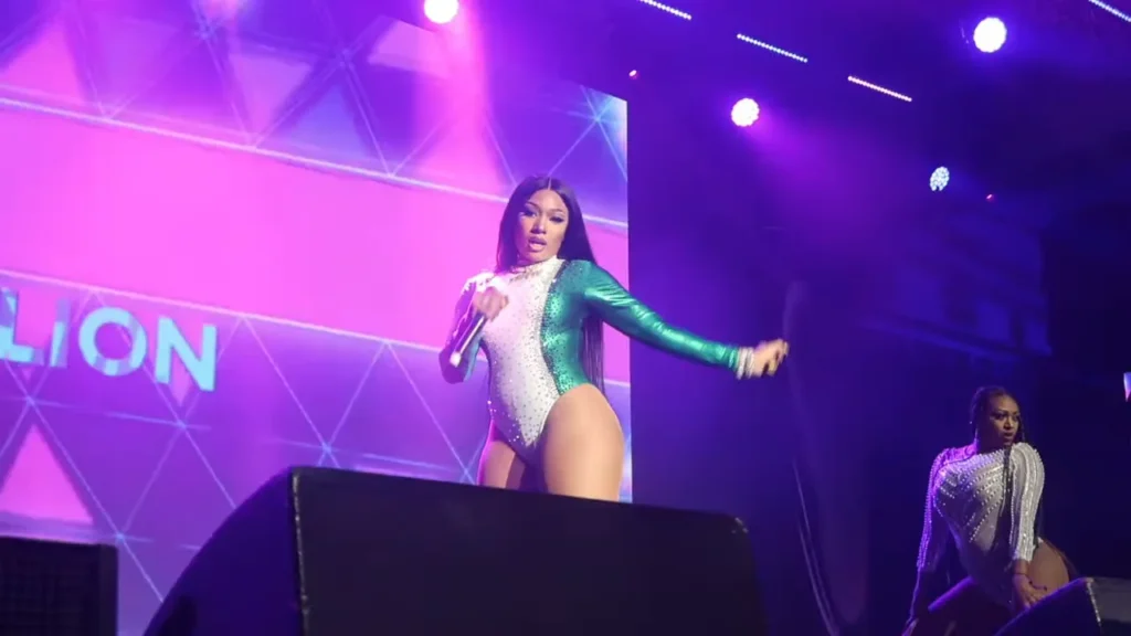 Megan Thee Stallion performing on stage in green and white bodysuit during concert tour