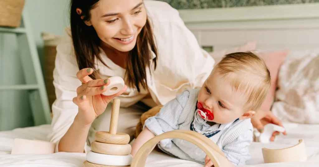 Baby on tummy time reaching for wooden toy while mother watches