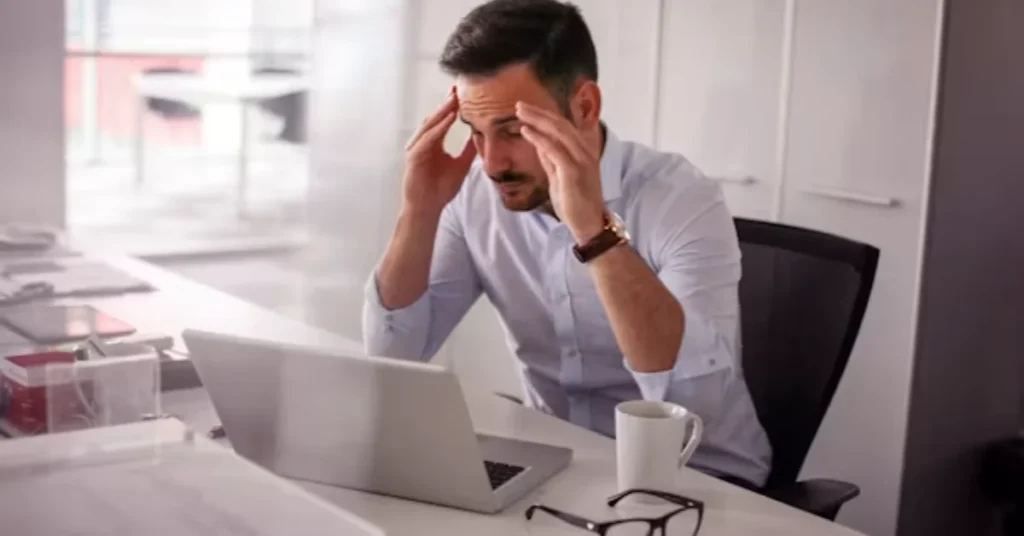 Man rubbing his temples with eye strain while working at laptop in office