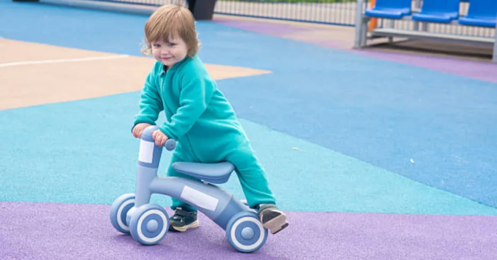Toddler riding a balance bike on a colorful playground surface.