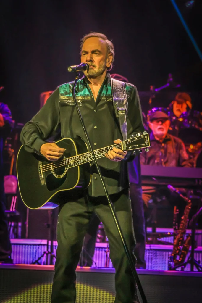 Neil Diamond performing live with his black acoustic guitar on stage