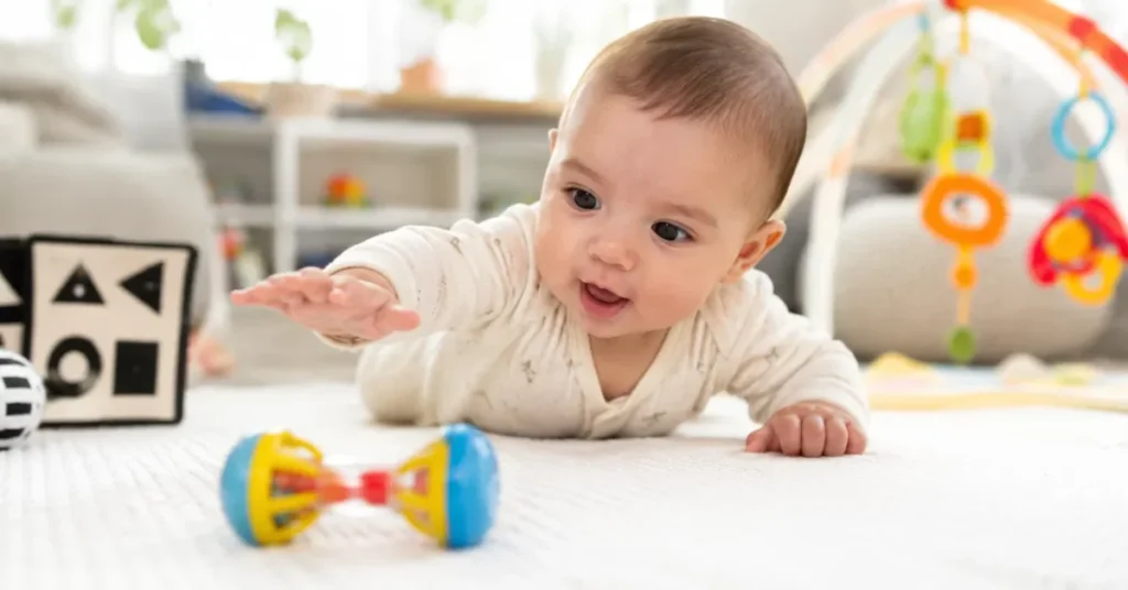 Baby in tummy time reaching hand toward colorful rattle toy