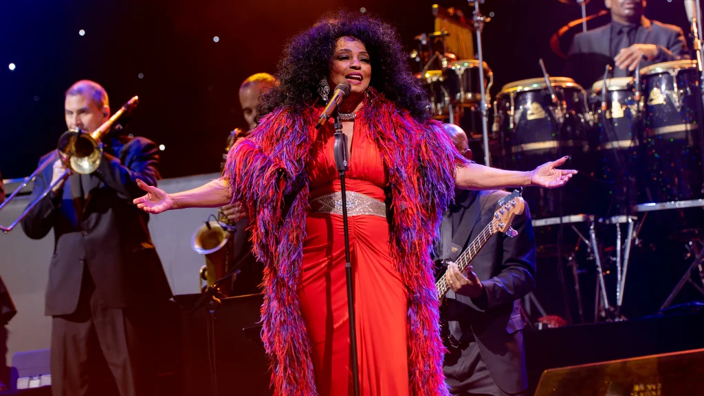 Diana Ross performing on stage in white sequined gown with microphone