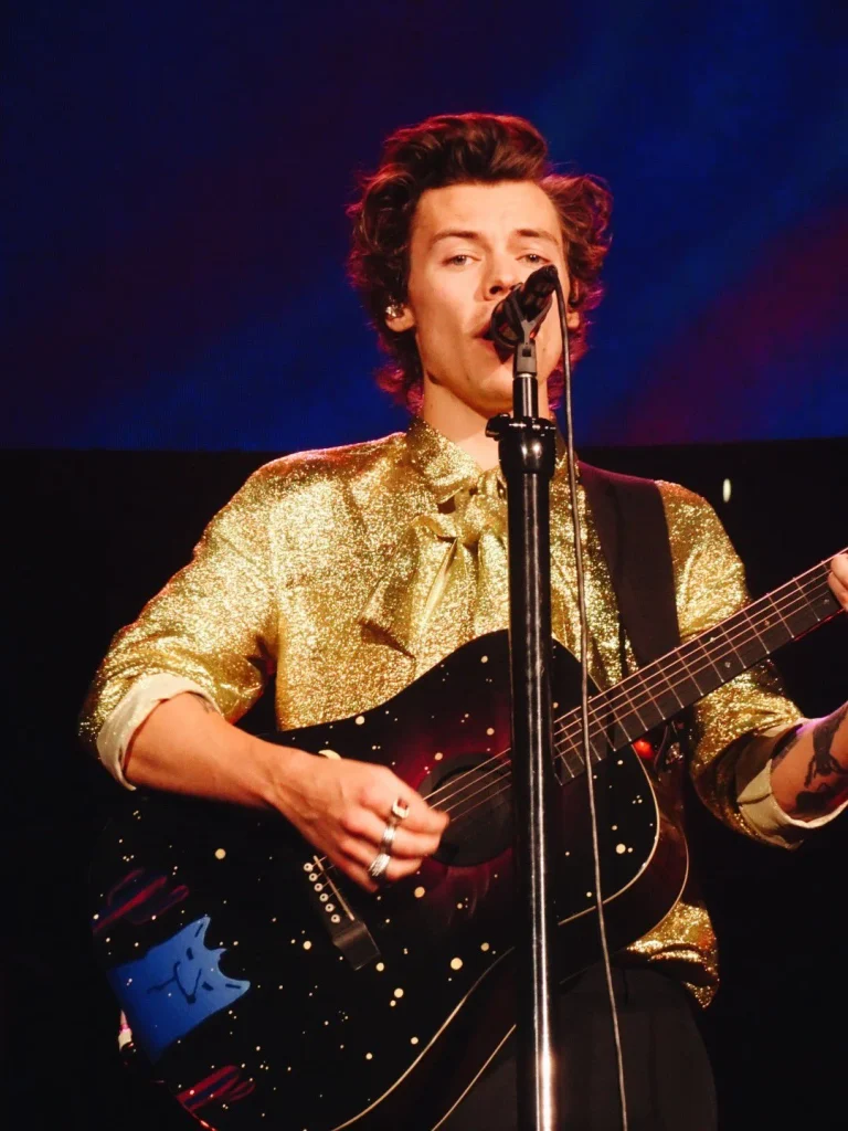 Harry Styles performing live on tour in gold sequined shirt playing guitar